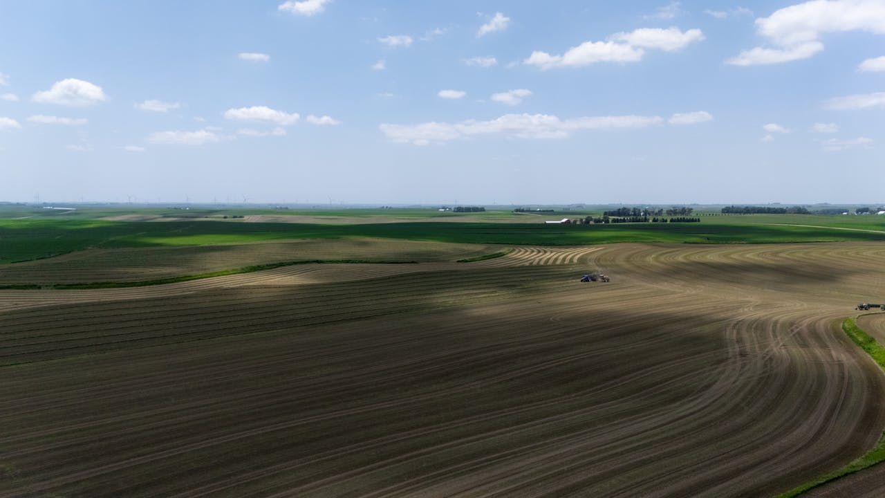 Aerial view of expansive farm fields with a tractor during summer harvest.